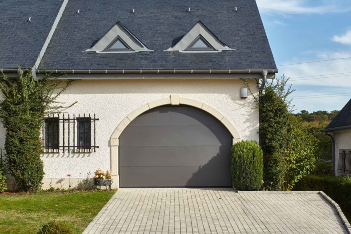 Rechte Seite der Vorderseite eines weißen Einfamilienhauses mit Blick auf ein graues Coplaning Alu Garagentor.