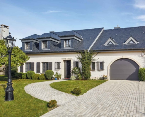 Weißes Einfamilienhaus mit grauer Coplaning Keramik Haustür, braunen Coplaning Holz- Alu Fenster und einem grauen Deckensektionalen Garagentor.