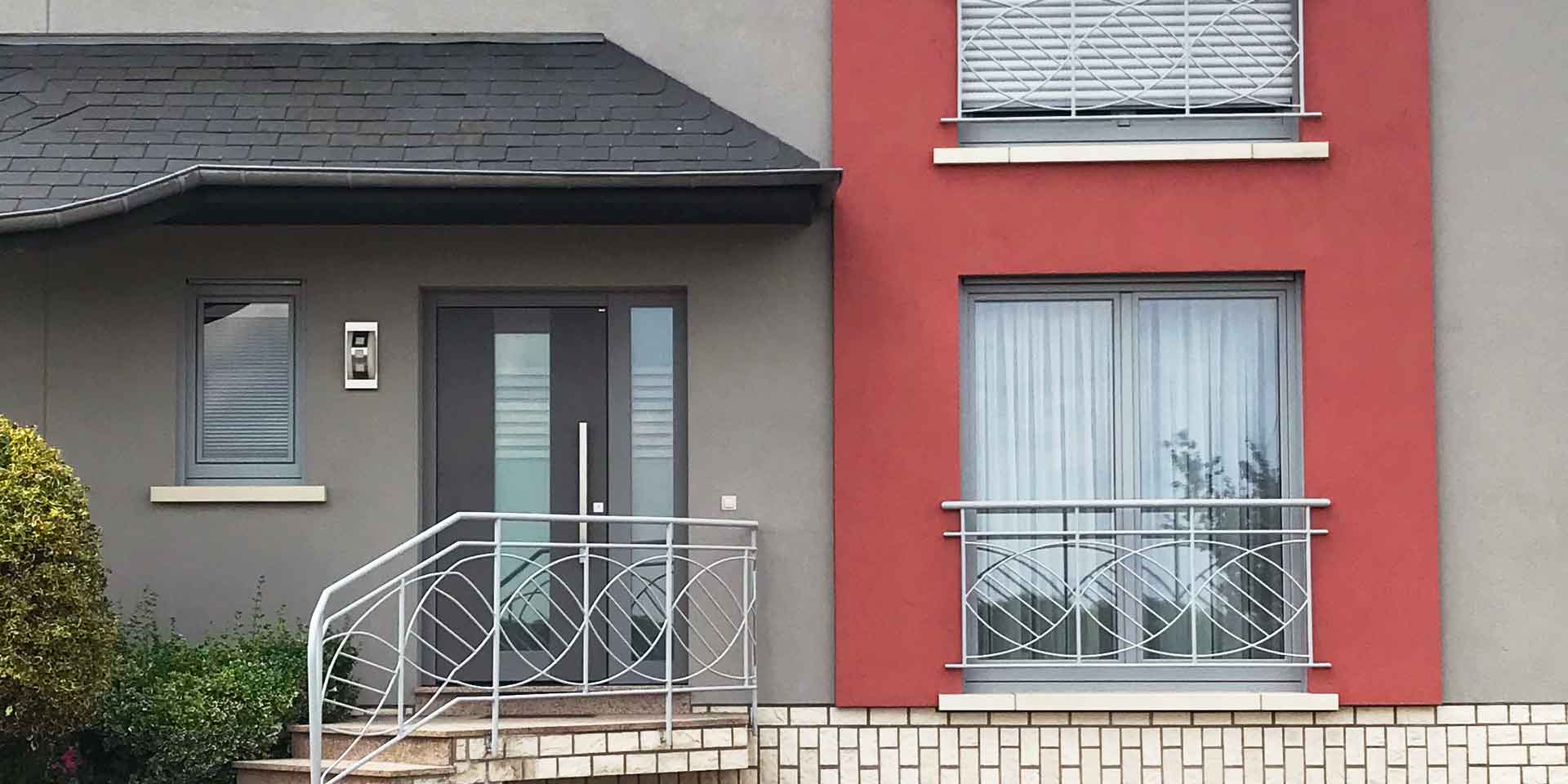 Nahaufnahme der Vorderseite eines grau- roten Einfamilienhauses mit einer grauen Coplaning Keramik Haustür.