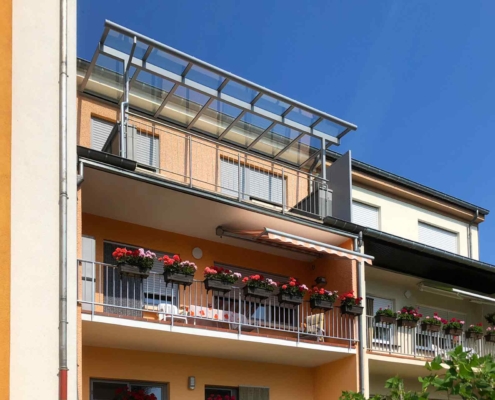 Oranges Einfamilienhaus mit einer grauen Coplaning Alu Balkon Überdachung mit Glasdach.
