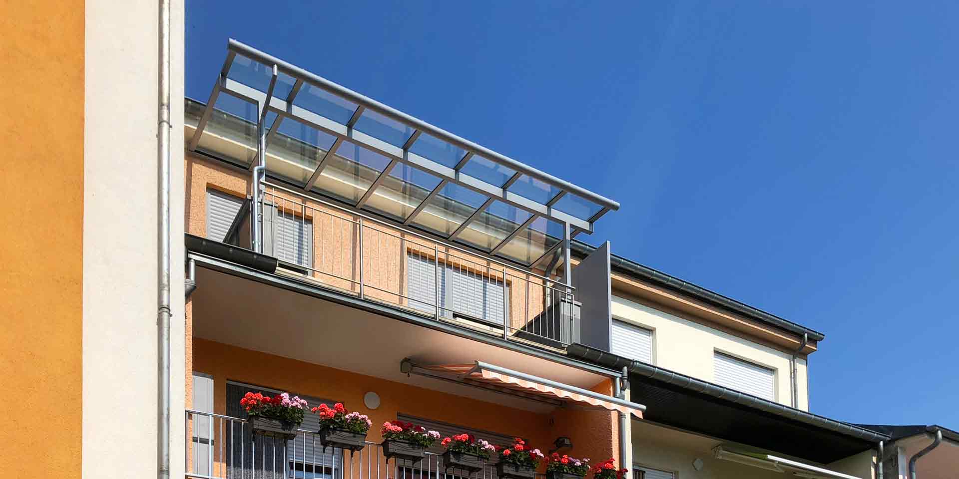Oranges Einfamilienhaus mit einer grauen Coplaning Alu Balkon Überdachung mit Glasdach.