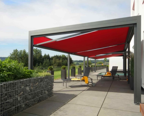 Weißes Einfamilienhaus mit einer Coplaning Veranda Pergola Terassenüberdachung mit grauem Quadrato und roten Markisen.