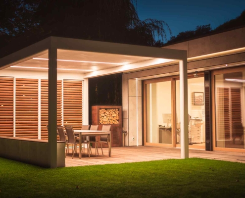Modernes Einfamilienhaus mit einem hochwertigen Coplaning Pergola in der Nacht mit moderner Terassenüberdachung eind einem Quadrato in weiß mit Lamellendach.