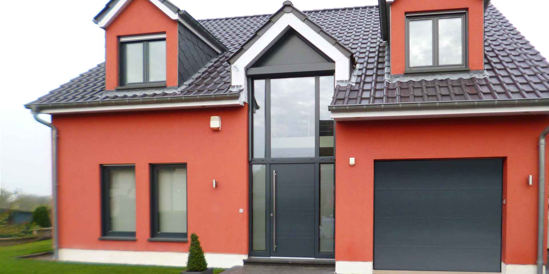 Rotes Einfamilienhaus mit grauer moderner Coplaning Haustür und grauen Coplaning Holz- Alu Fenster.