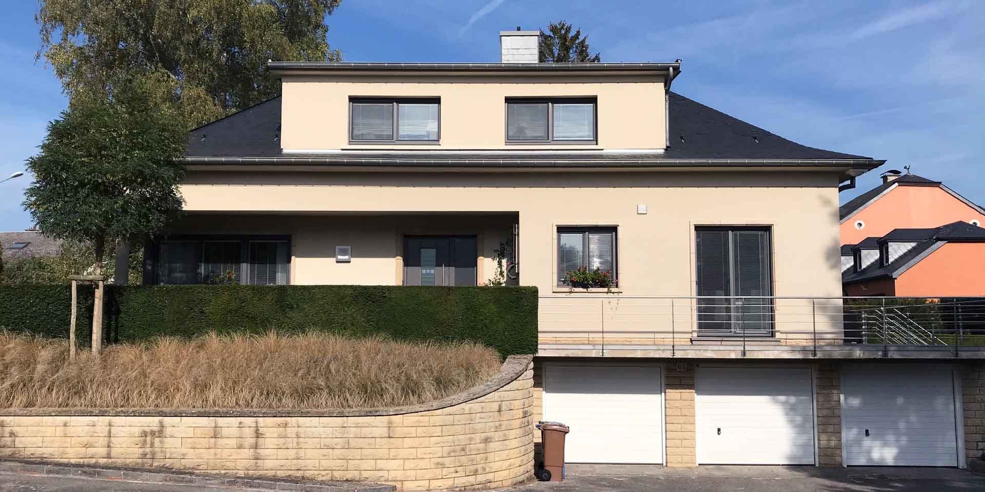 Beiges Einfamilienhaus mit grauen Coplaning PVC Alu-Fenster und einer grauen modernen Coplaning Haustür mit Seitenlicht aus Glas.