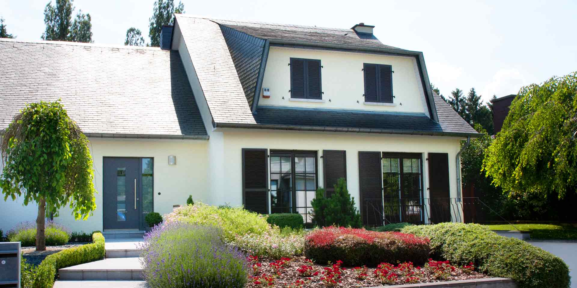 Weißes Einfamilienhaus mit grauen Coplaning Alu Fenster mit passenden Klappläden und einer grauen Coplaning Alu Haustür.