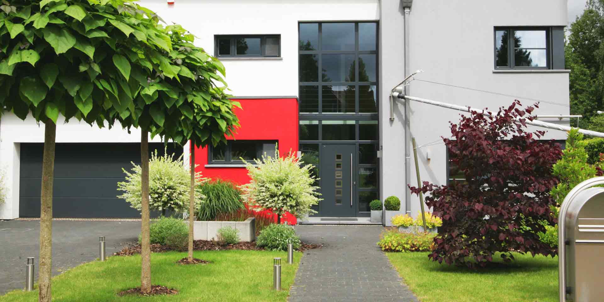 Rot- grau- weißes Einfamilienhaus mit moderner grauer Coplaning Haustür, grauen Coplaning Alu Fenster und einem grauen Coplaning Garagentor.