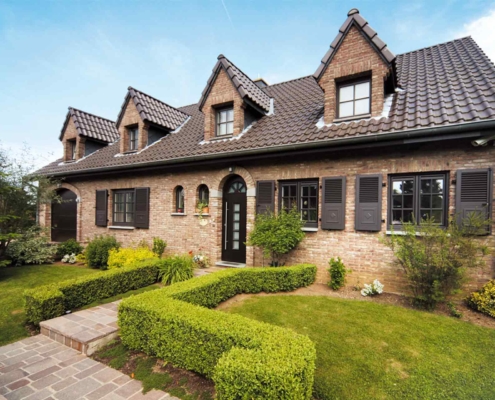 Einfamilienhaus mit Steinfassade mit brauner Coplaning Rundbogen Haustür und brauen Landhausstil klassischen einbruchsicheren Coplaning Gaubenfenster.