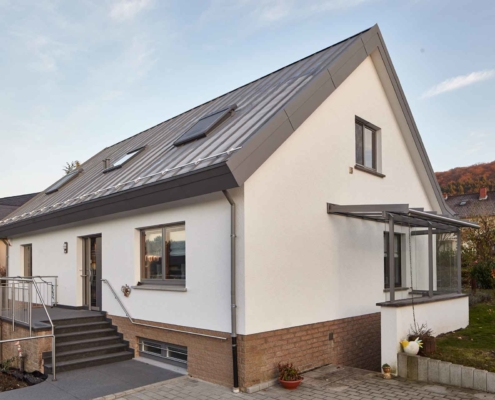 Weißes Einfamilienhaus von rechts gesehen mit einer neuen modernen grauen Coplaning Haustür und grauen Coplaning Holz Alu Fenster.
