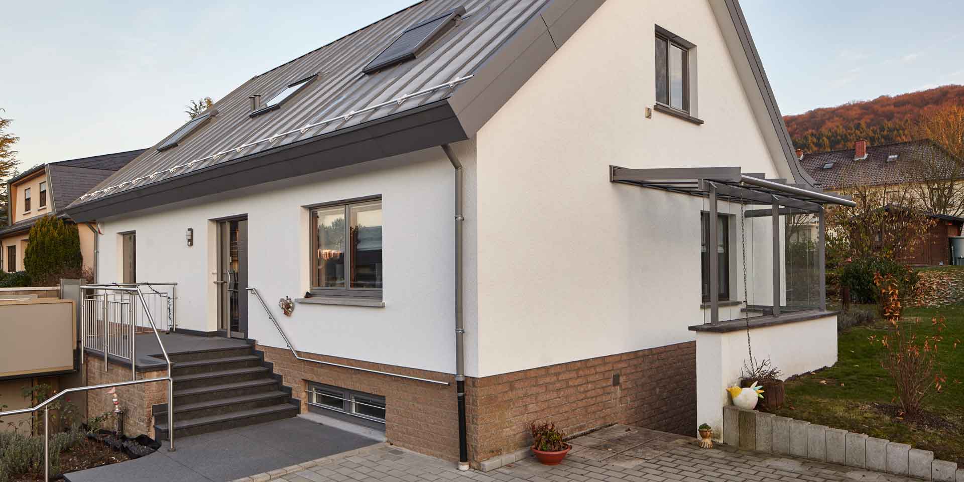 Weißes Einfamilienhaus von rechts gesehen mit einer neuen modernen grauen Coplaning Haustür und grauen Coplaning Holz Alu Fenster.