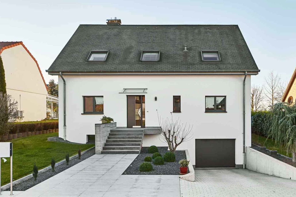 Weißes Einfamilienhaus mit einer grauen Coplaning Haustür, grauen einbruchsicheren Coplaning Alu Fenster und einem grauen Garagentor.