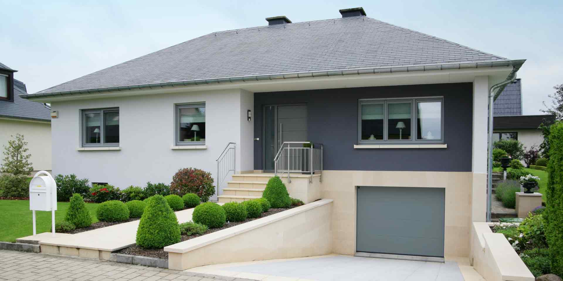 Weiß- graues Einfamilienhaus mit grauer Coplaning Haustür mit Glasseitenteil und grauen Coplaning Alu Jalousiefenster.