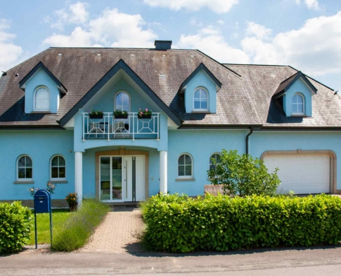 Blaues Einfamilienhaus mit weißer Coplaning Haustür und weißen Coplaning runden Fenster.