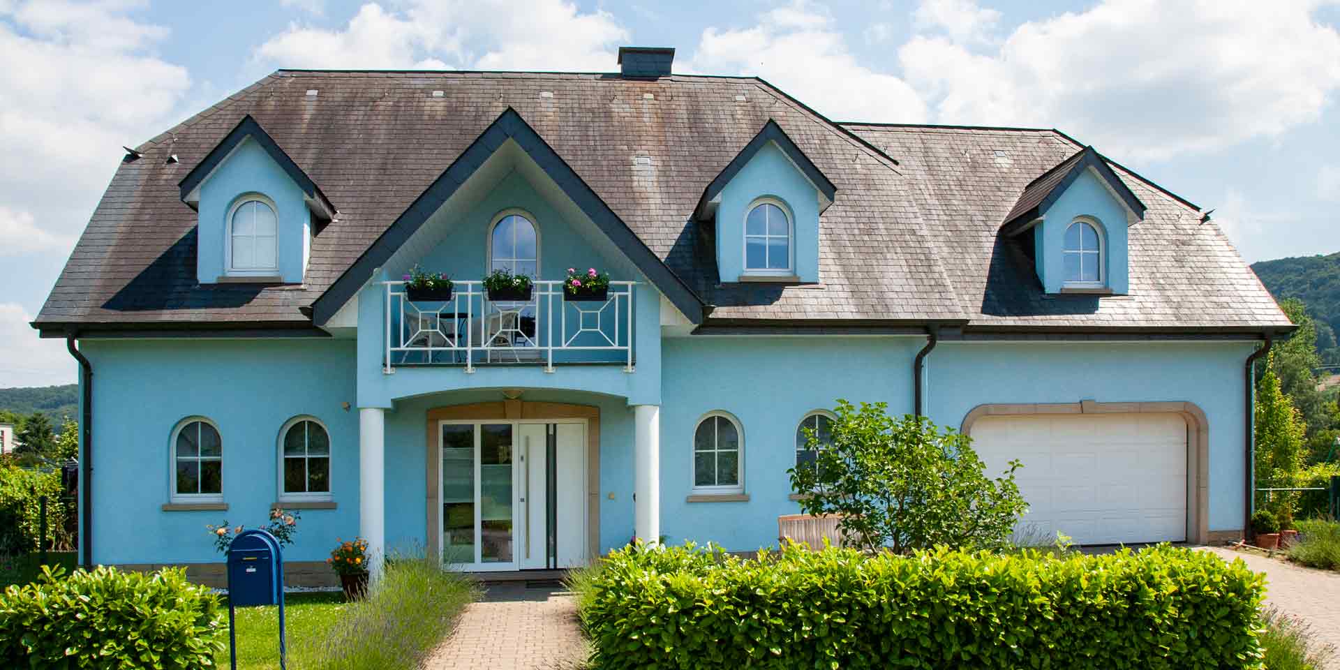 Blaues Einfamilienhaus mit weißer Coplaning Haustür und weißen Coplaning runden Fenster.