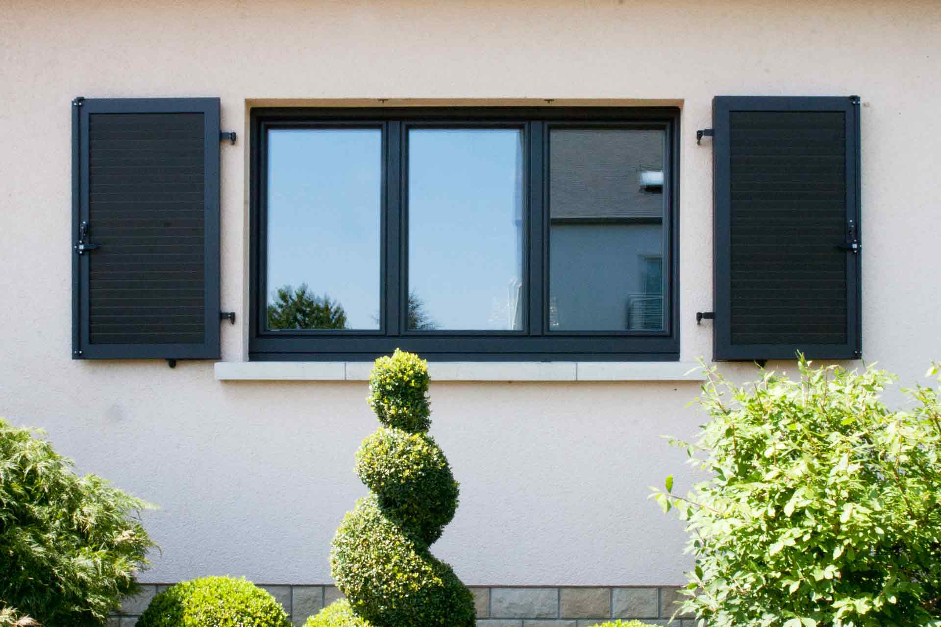Nahaufnahme von einem modernen grauen Coplaning Fenster mit grauen Klappläden des leicht pinken Einfamilienhauses.