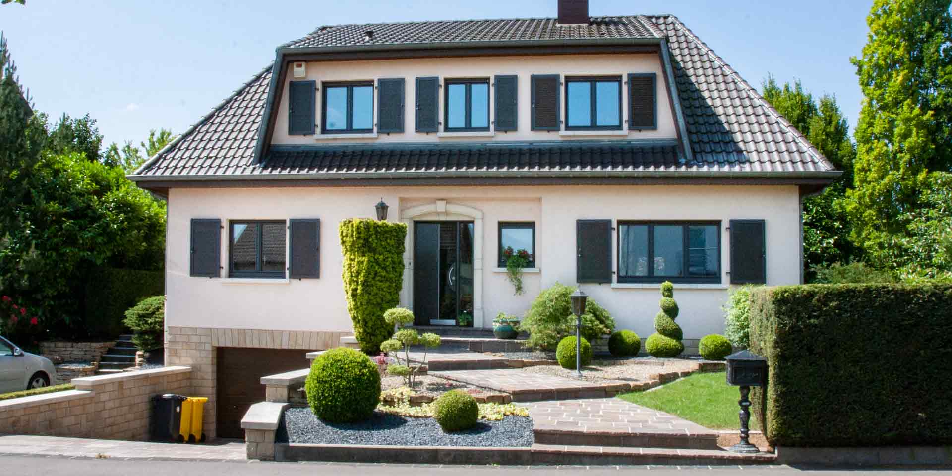 Leicht pinkes Einfamilienhaus mit moderner grau- schwarzen Coplaning Haustür,grauen Coplaning Fenster mit grauen Klappläden und mit einem Garagentor.