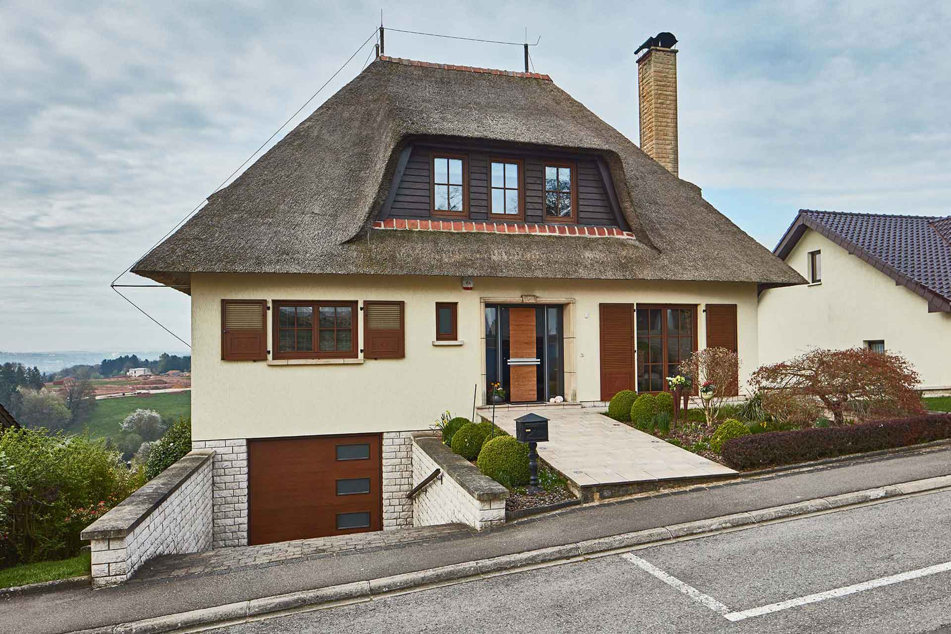 Weißes Einfamilienhaus mit Coplaning Holz- Glas Haustür, Coplaning Holz- Alu Fenster und ein Garagentor mit Holzoptik.