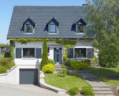 Weißes Einfamilienhaus mit neuen modernen Haustür und grauen einbruchsicheren Coplaning Fenster und einem grauen Garagentor.