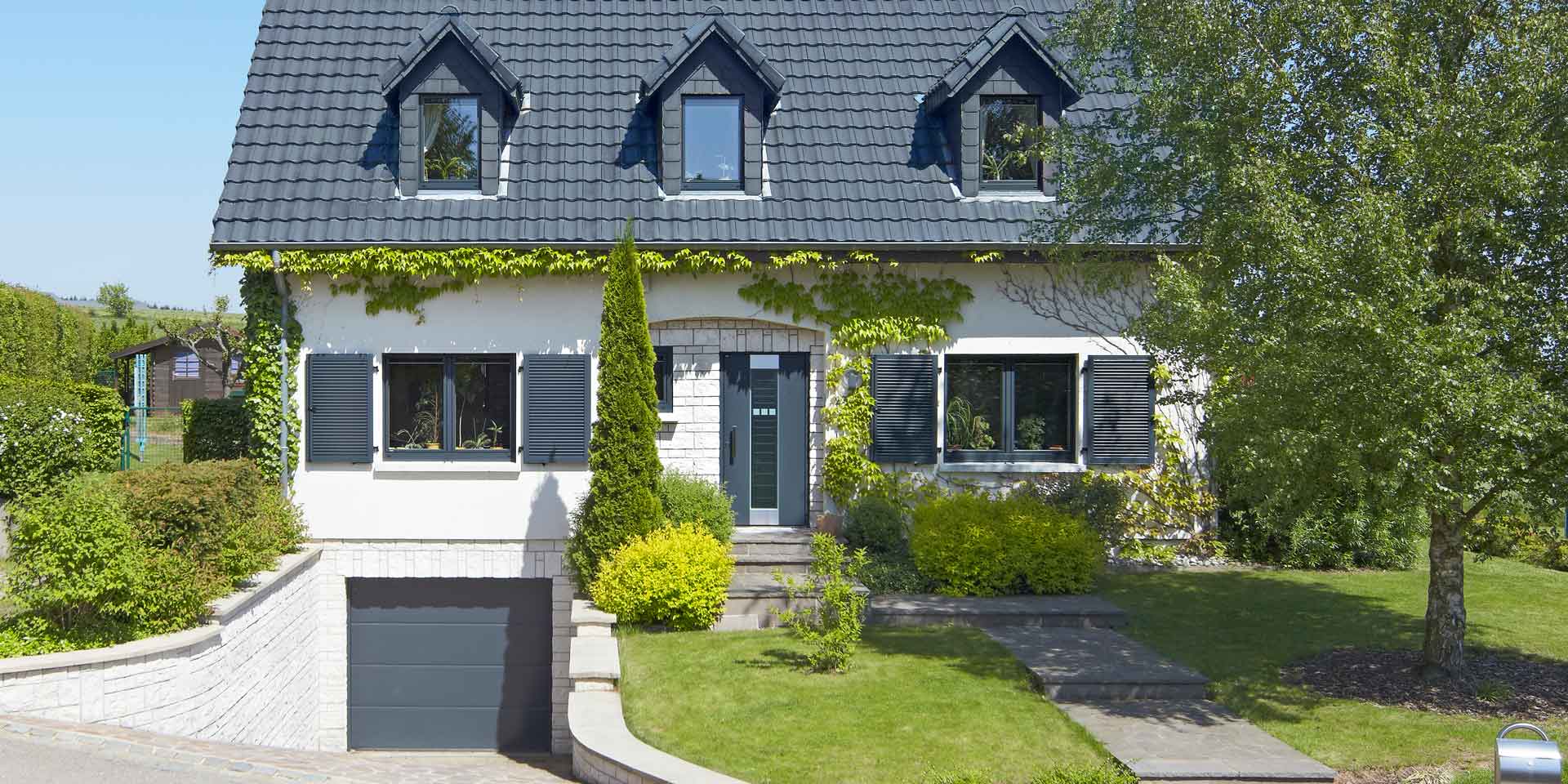 Weißes Einfamilienhaus mit neuen modernen Haustür und grauen einbruchsicheren Coplaning Fenster und einem grauen Garagentor.