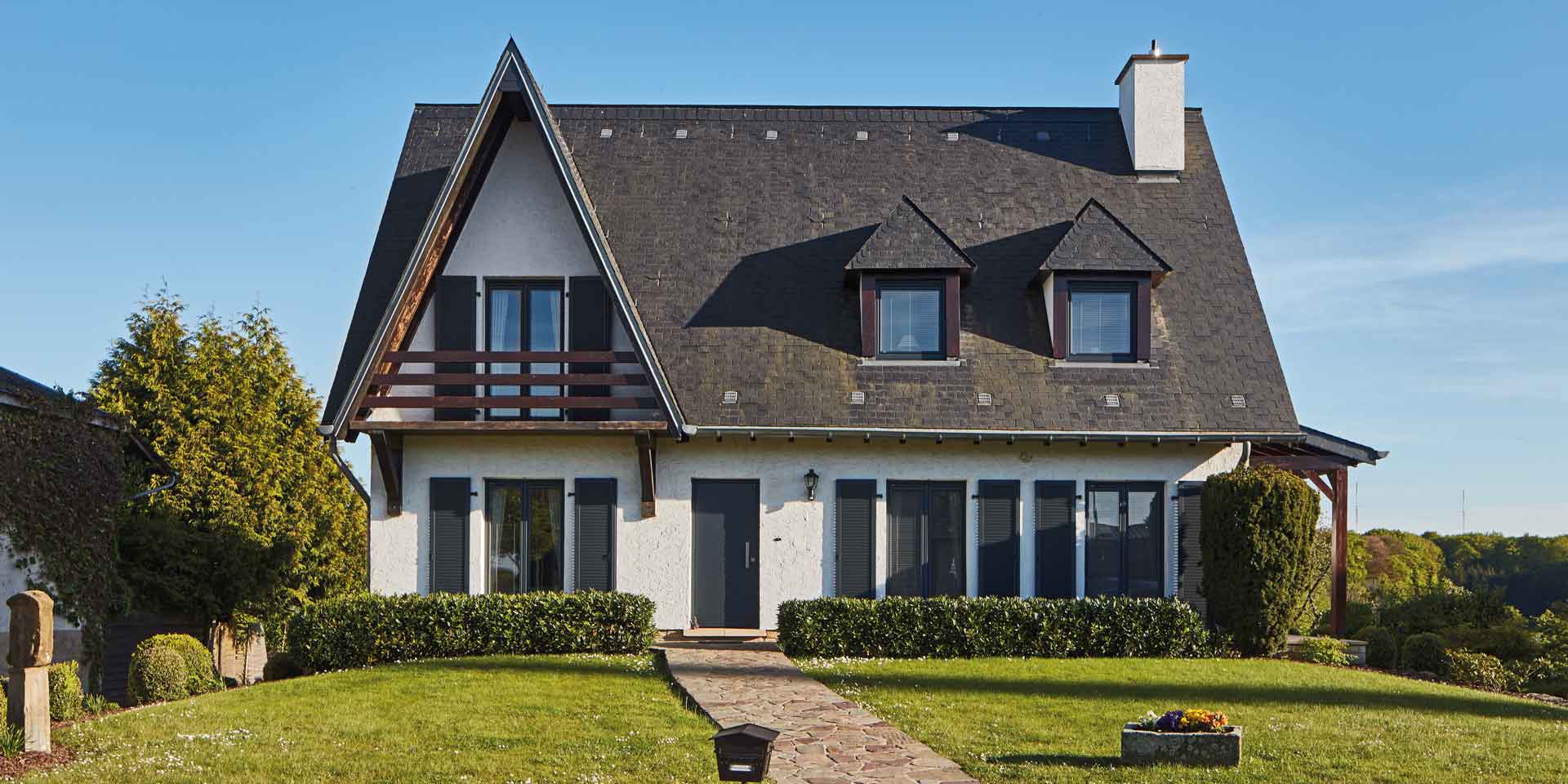 Weißes Einfamilienhaus mit einer grauen Coplaning Alu Haustür und grauen Coplaning Holz- Alu PVC Fenster mit passenden Klappläden.
