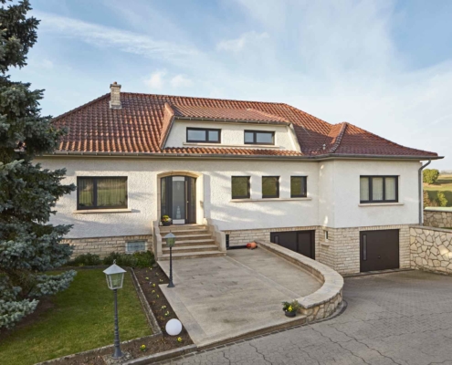 Weißes Einfamilienhaus in Emerange mit einer grauen Coplaning Alu Haustür mit Seitenteilen aus Glas und grauen Coplaning Alu Fenster.