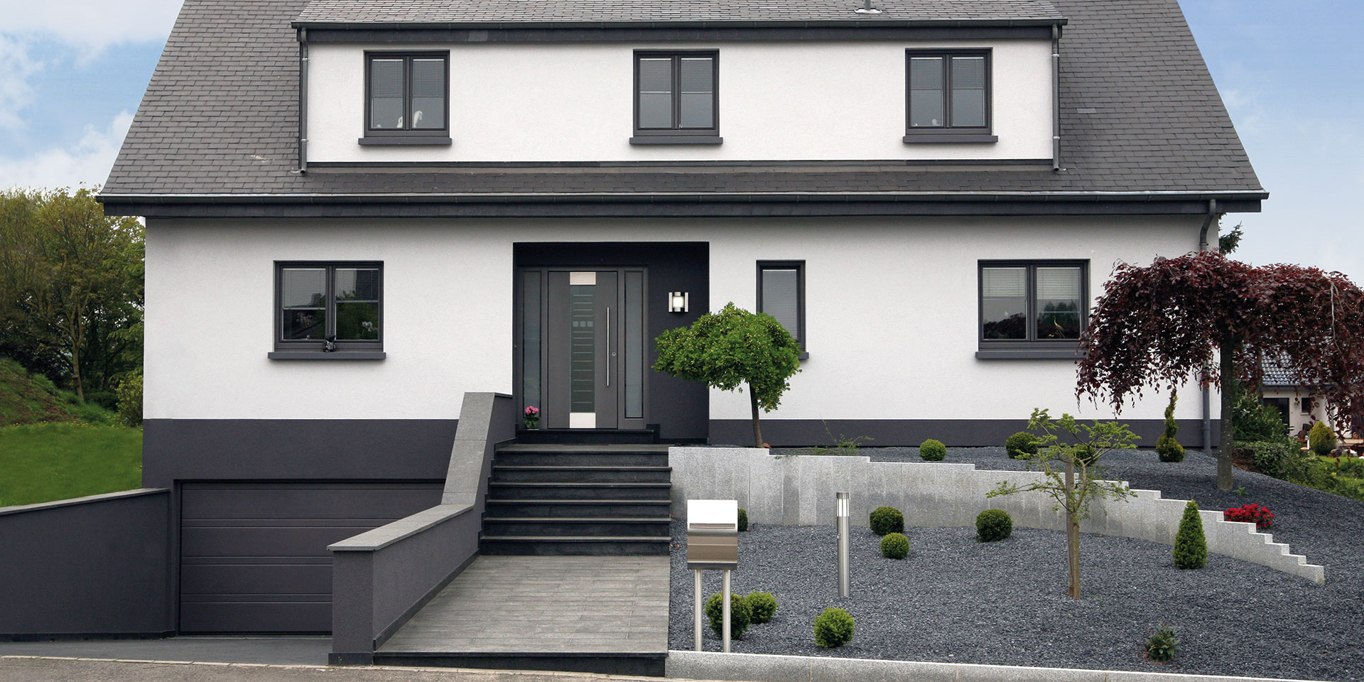 Modernes grau-weißes Einfamilienhaus mit grauer moderner Coplaning Haustür und grauen Coplaning Fenster.