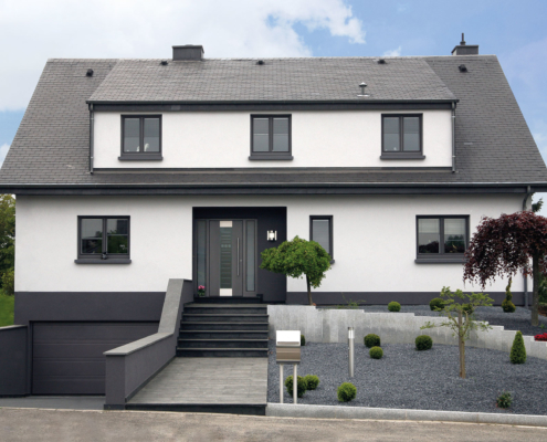 Modernes grau-weißes Einfamilienhaus mit grauer moderner Coplaning Haustür und grauen Coplaning Fenster.