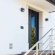Nahaufnahme des Eingangsbereichs eines weißen Einfamilienhauses mit Blick auf eine neue moderne graue Coplaning Haustür mit großem Lichtausschnitt.