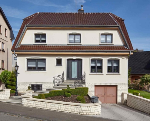 Weißes Einfamilienhaus mit grauer moderner Coplaning Haustür und grauen Coplaning Alu Fenster.