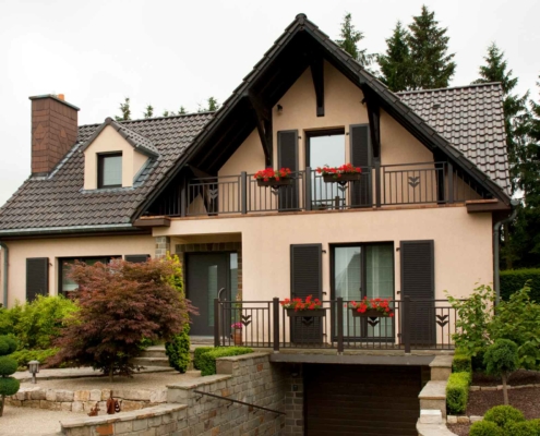 Leicht pinkes Einfamilienhaus mit einer braunen Coplaning Alu Lack Haustür, braunen Coplaning Alu Fenster mit braunen Alu Klappläden.