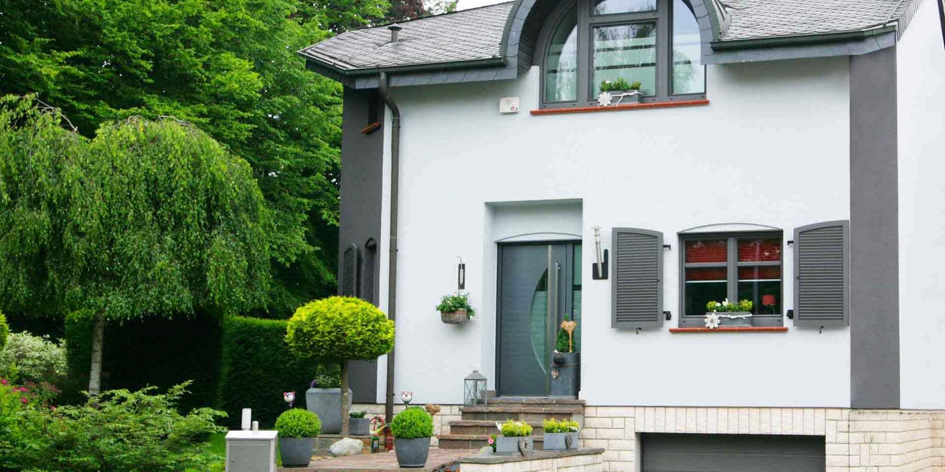 Weiß- graues Einfamilienhaus mit moderner grauer Coplaning Haustür, grauen Coplaning Alu Fenster und einem grauen Coplaning Garagentor.