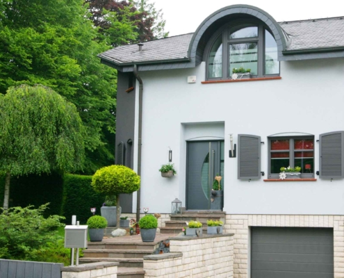 Weiß- graues Einfamilienhaus mit moderner grauer Coplaning Haustür, grauen Coplaning Alu Fenster und einem grauen Coplaning Garagentor.