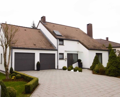 Weißes Einfamilienhaus mit einer grauen Coplaning Alu Haustür, grauen Coplaning Jalousienfenster und einem grauen Coplaning Garagentor.