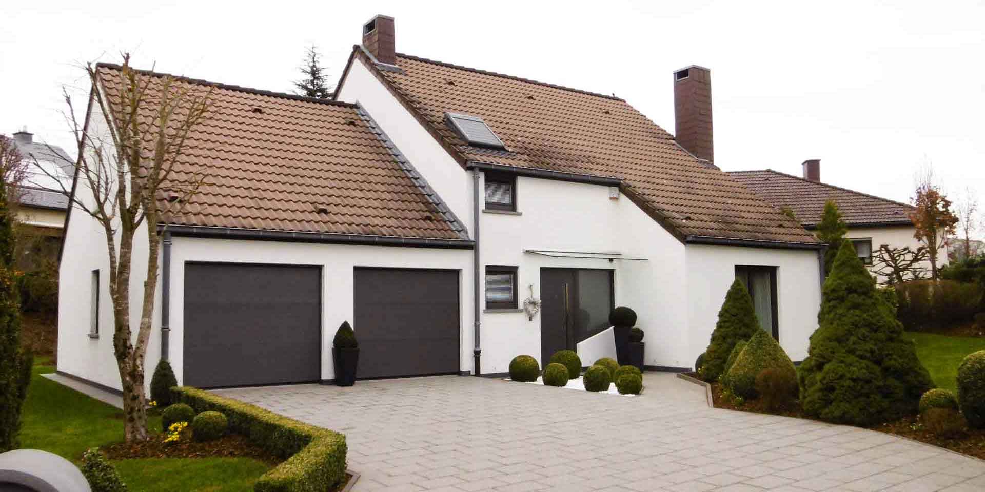 Weißes Einfamilienhaus mit einer grauen Coplaning Alu Haustür, grauen Coplaning Jalousienfenster und einem grauen Coplaning Garagentor.