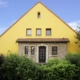 Gelbes Einfamilienhaus mit brauner Coplaning Haustür und braunen Coplaning Holz Jalousiefenster.