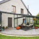 Graues Einfamilienhaus mit einer grauen Coplaning Aluminium Veranda Glasfaltwand mit Terassenüberdachung.