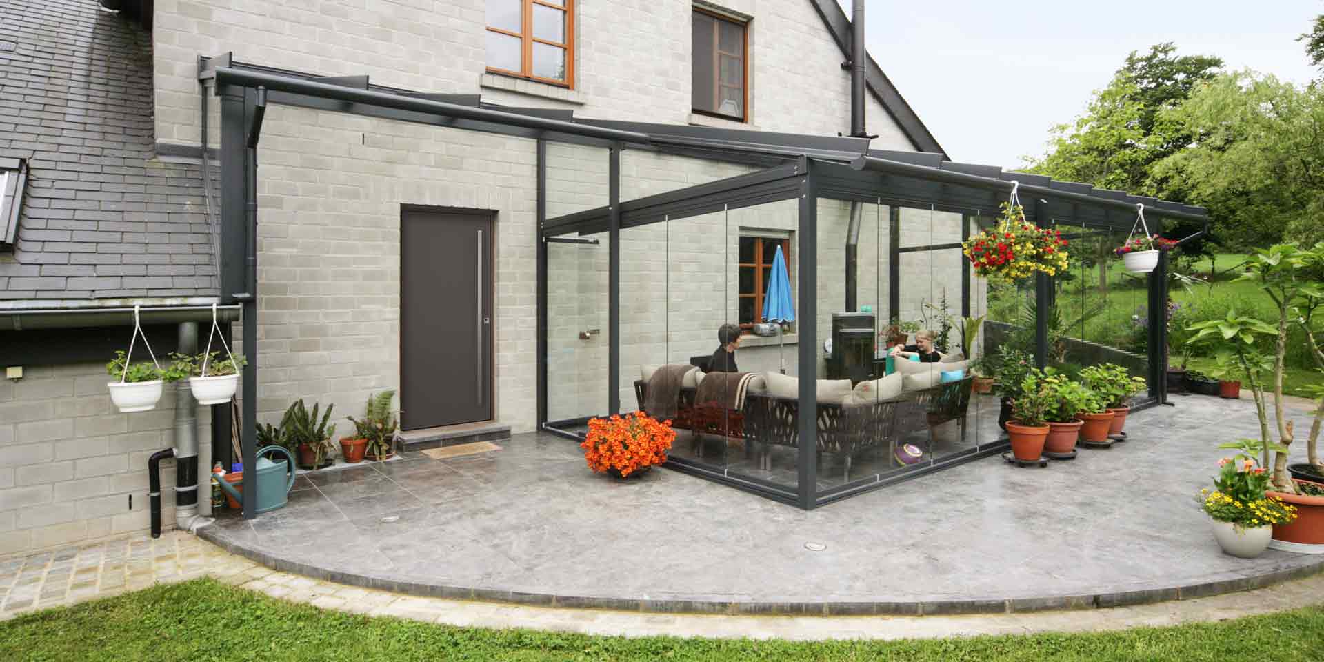 Graues Einfamilienhaus mit einer grauen Coplaning Aluminium Veranda Glasfaltwand mit Terassenüberdachung.