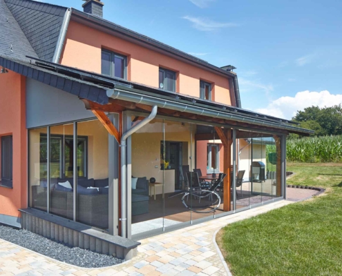 Oranges Einfamilienhaus mit Nahaufnahme der Rückseite des Hauses mit Blick auf ein Coplaning Terassen Wintergarten mit einer grauen Coplaning Glasfaltwand ohne Rahmenprofile.