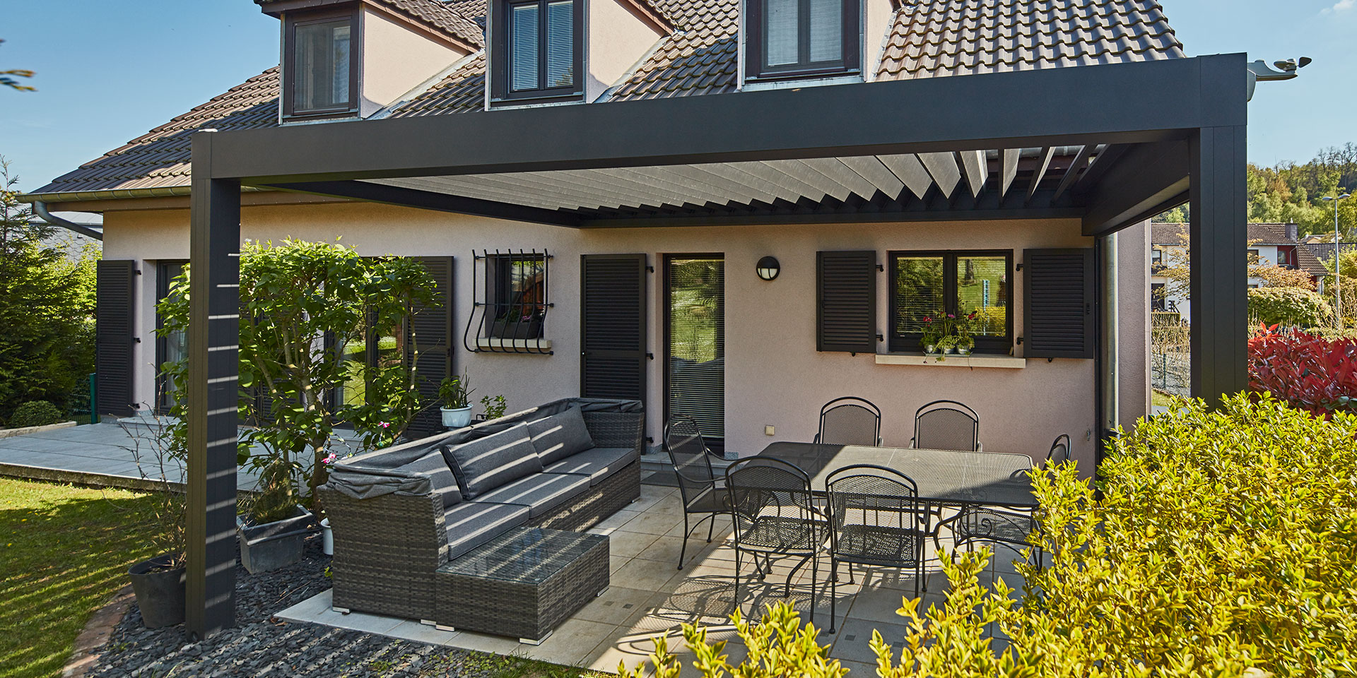 Rückseite des leicht pinken Einfamilienhauses in Dudelange mit einem grauen Coplaning Aluminium Quadrato mit offenen Lamellendach.