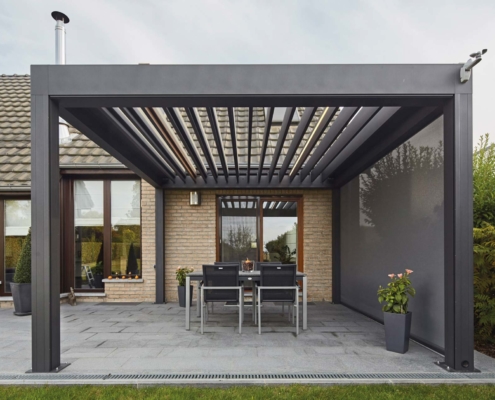 Einfamilienhaus mit Steinfassade mit einem grauen Coplaning Veranda Quadrato mit Terassenüberdachung und einem Lamellendach aus Aluminium mit Windschutz.