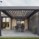 Einfamilienhaus mit Steinfassade mit einem grauen Coplaning Veranda Quadrato mit Terassenüberdachung und einem Lamellendach aus Aluminium mit Windschutz.