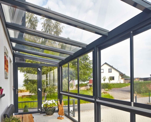 Nahaufnahme des inneren der grauen Coplaning Veranda Überdachung aus Aluminium und mit grauem Balkon mit Treppenbereich und Verglasung mit Schiebefenster.