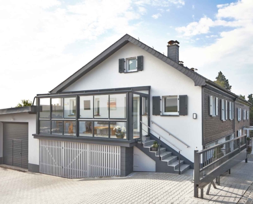 Weißes Einfamilienhaus mit einer Coplaning Veranda Überdachung aus Aluminium, grauem Balkon mit Treppenbereich und einer Verglasung mit Schiebefenster und integrierter Beleuchtung.Weißes Einfamilienhaus mit einer Coplaning Veranda Überdachung aus Aluminium, grauem Balkon mit Treppenbereich und einer Verglasung mit Schiebefenster und integrierter Beleuchtung.