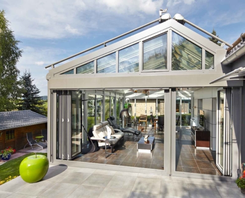 Einfamilienhaus mit Steinfassade mit Nahaufnahme der Rückseite des Hauses mit Blick auf ein Coplaning Veranda Wintergarten mit geöffneter hellgrauer Aluminium Faltanlage und Glasdach.