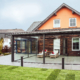 Oranges Einfamilienhaus mit einer Coplaning Veranda verglasten Terasse mit grauer Alu- Innenmarkise und integrierter Beleuchtung.