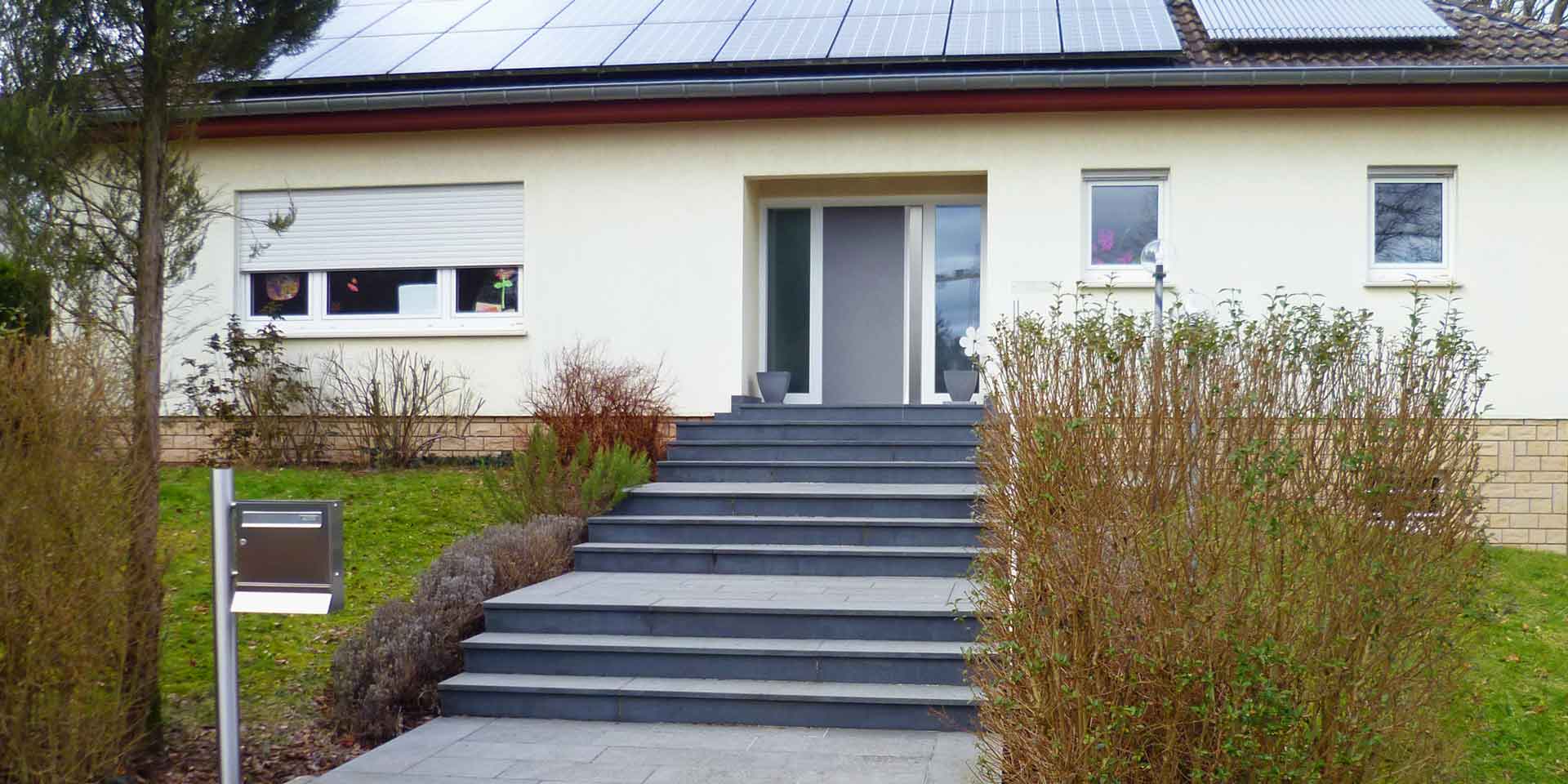Gelbliches Einfamilienhaus mit moderner grauer Coplaning Haustür und weißen Coplaning Fenstern.