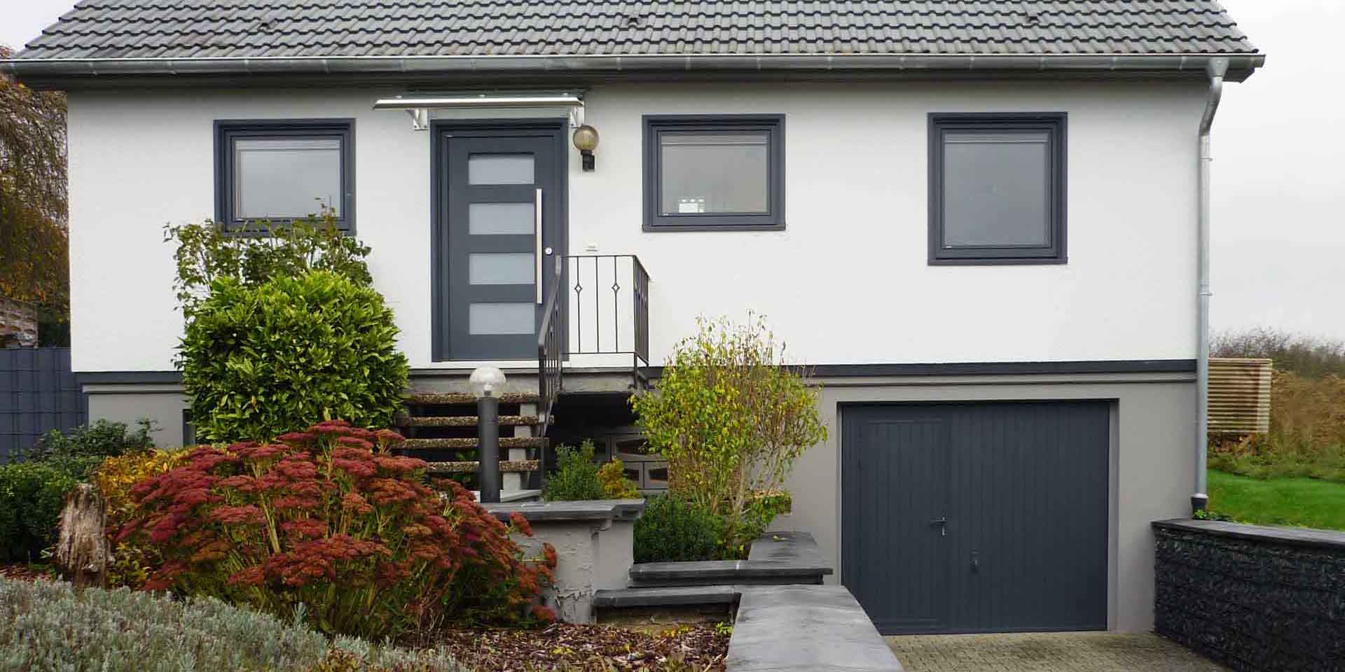 Weißes Einfamilienhaus mit moderner grauer Coplaning Haustür und grauen Coplaning Holz- Alu Fenster.