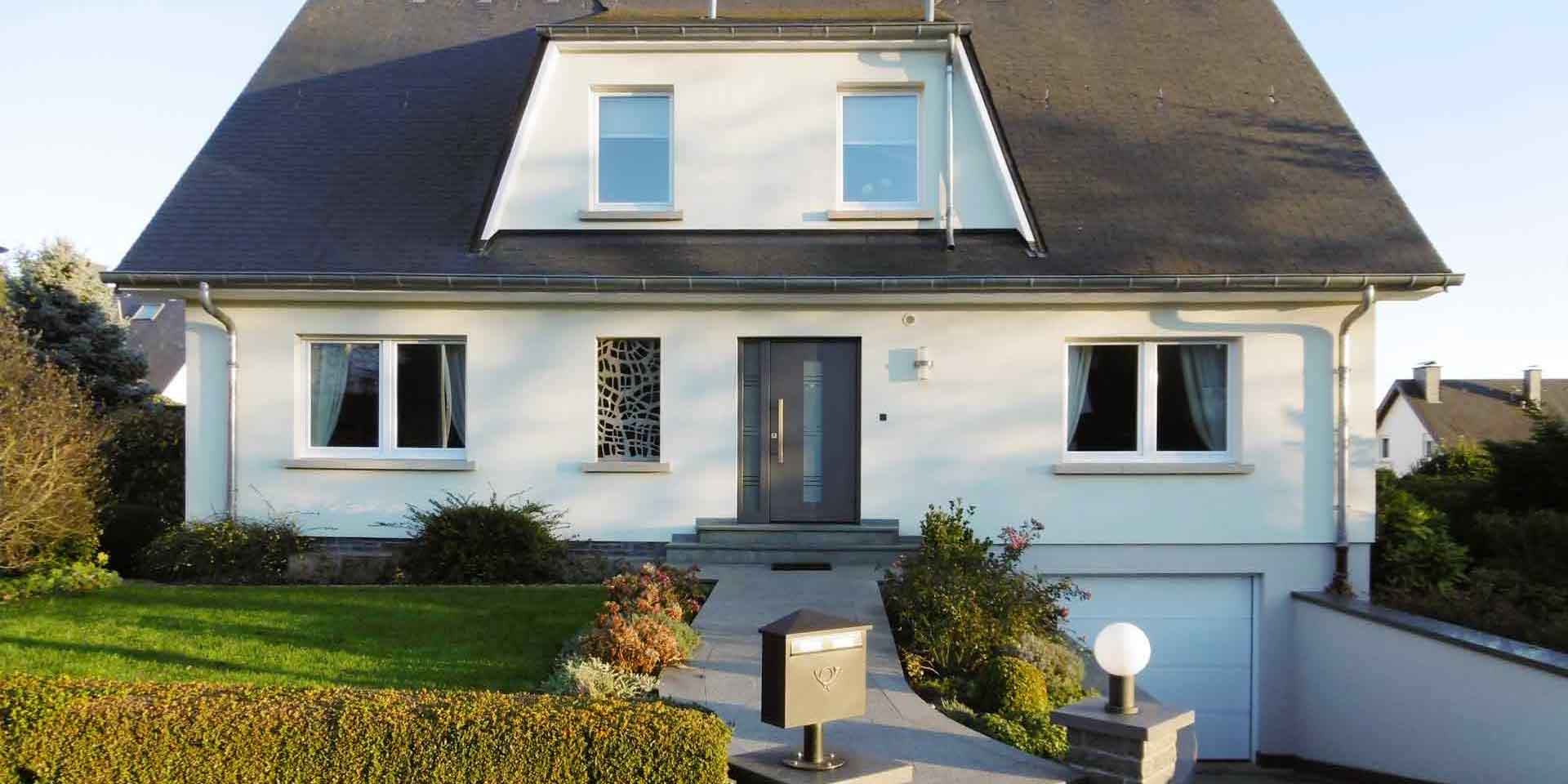 Weißes Einfamilienhaus mit einer grauen Coplaning Lack Haustür.