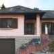 Vorderseite eines leicht pinken Einfamilienhauses mit brauner modernen Coplaning Haustür und braunen Fensterläden.