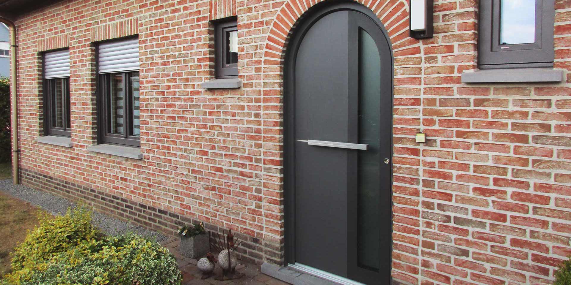 Nahaufnahme des Eingangsbereichs eines Einfamilienhauses mit Steinfassade mit einer modernen grauen Coplaning Haustür.